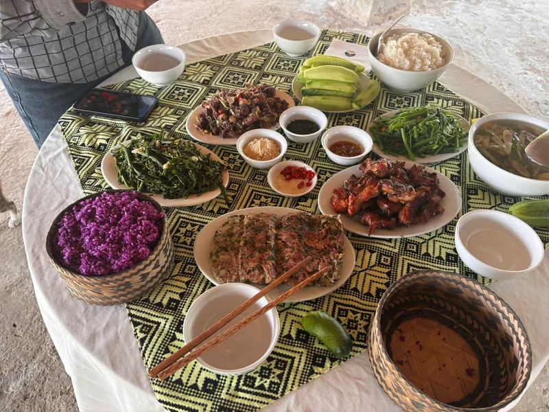 A round table in Dien Bien Phu spread with grilled meat, purple sticky rice, fried fish, and local dishes on woven baskets.