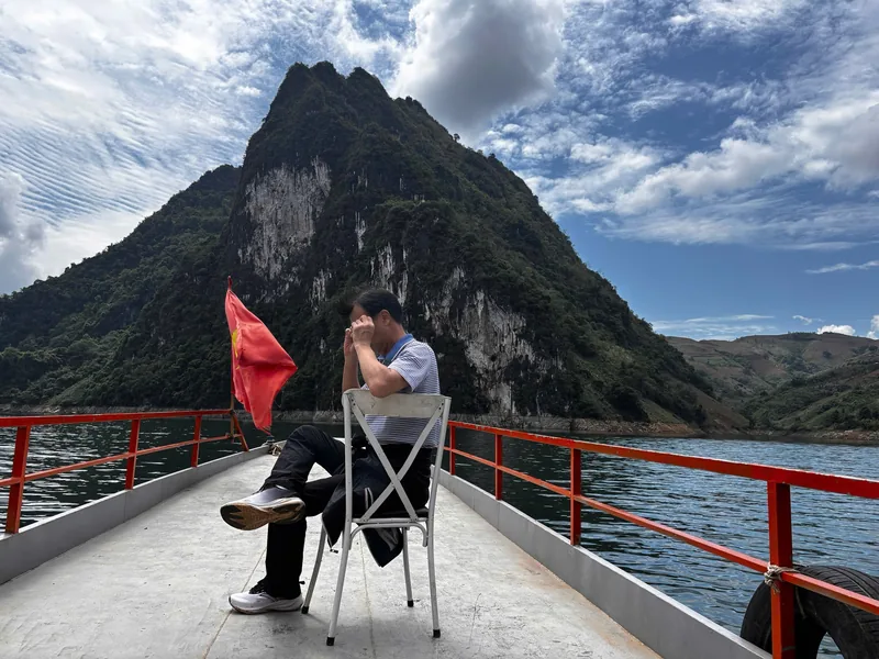 A man sits on a boat deck admiring a limestone peak rising from a reservoir near Dien Bien Phu.