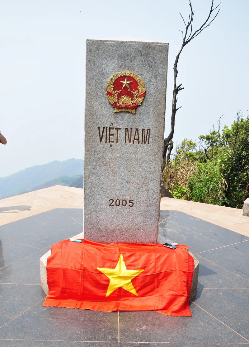 A stone border marker inscribed 'Việt Nam 2005' draped with a national flag atop A Pa Chải summit in Điện Biên.