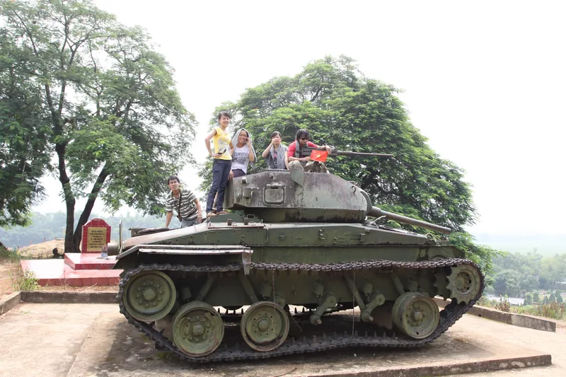 Visitors pose atop a preserved war-era tank at a Dien Bien Phu historical monument site.