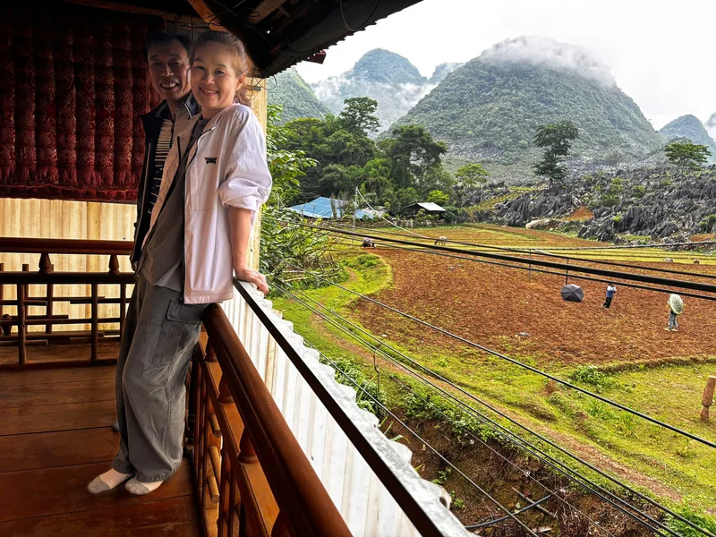 Two visitors smile on a wooden balcony overlooking terraced fields and karst mountains near Dien Bien Phu.