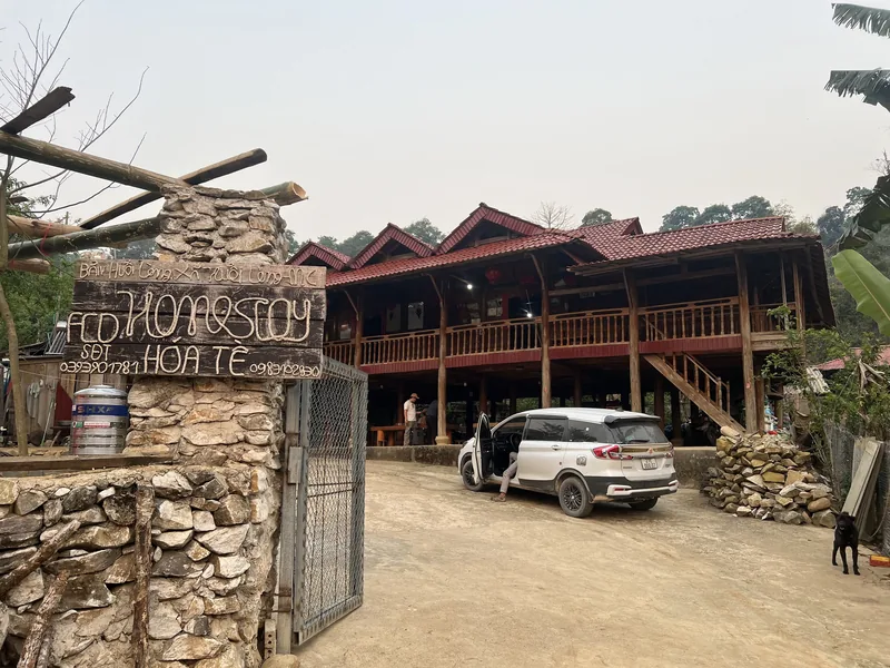 A wooden stilt-house homestay with a red tiled roof and stone gate stands in a rural area of Dien Bien.