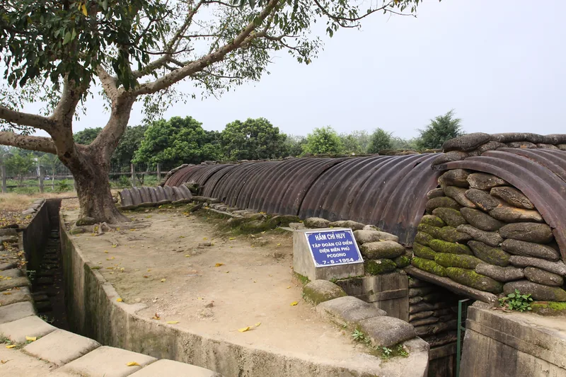 Corrugated metal bunkers with sandbags and a sign mark the command post ruins in Dien Bien Phu.