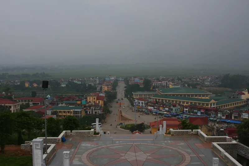 An elevated view overlooks the town of Dien Bien under a hazy grey sky, with rooftops stretching toward green fields.