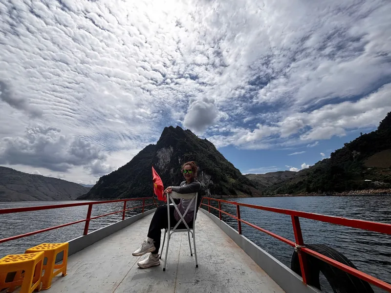 A woman sits on the bow of a boat crossing a reservoir surrounded by karst mountains near Dien Bien Phu.