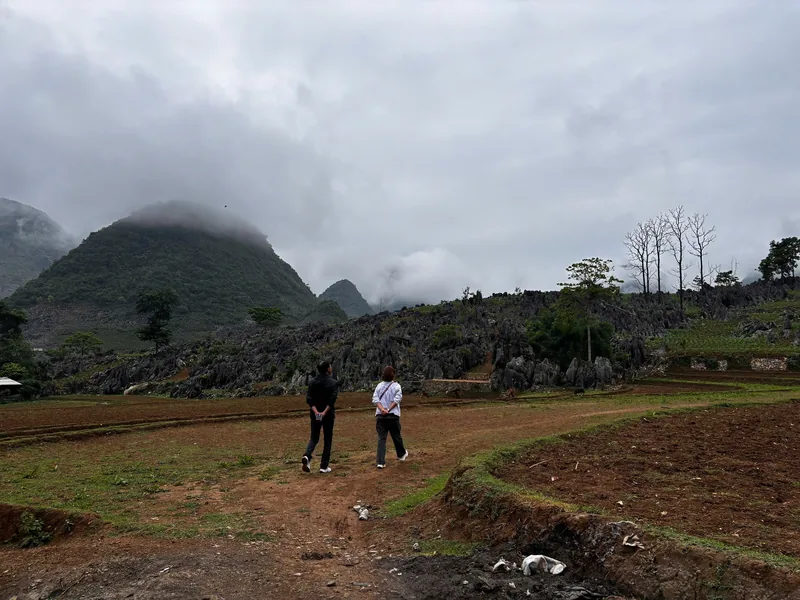 Two travelers walk across a rocky plateau beneath misty mountains near Dien Bien Phu, Vietnam.