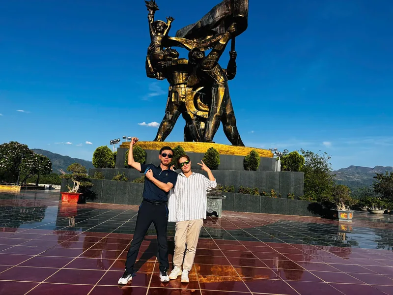 Two men pose for a photo beneath a large bronze war memorial statue in Dien Bien Phu.