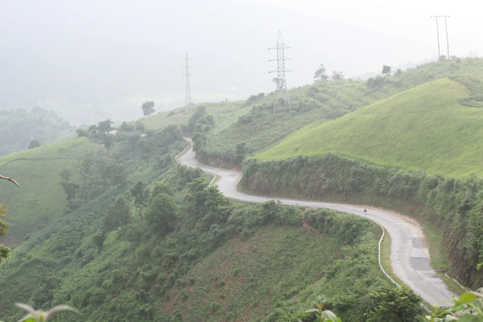 A winding mountain road curves through misty green hills near A Pa Chai in Dien Bien province.