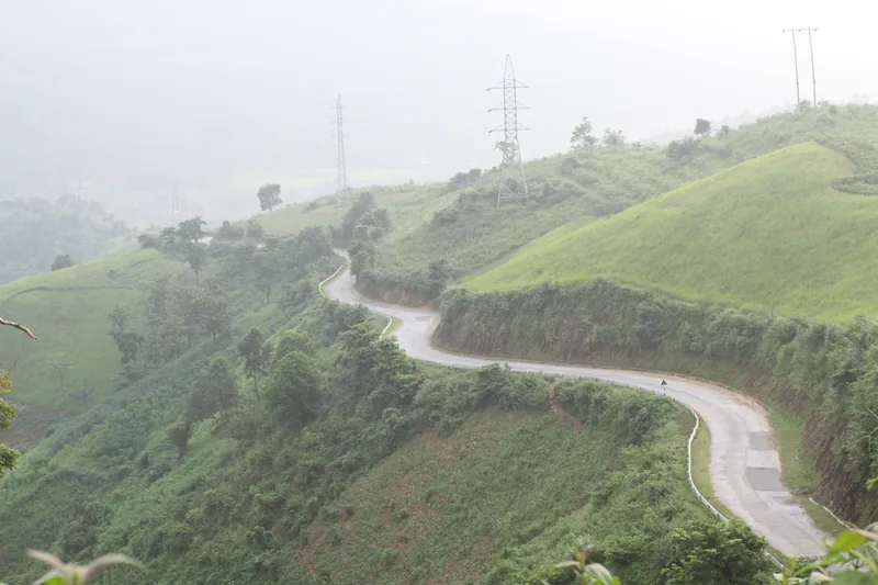 A winding mountain road curves through misty green hills near A Pa Chai in Dien Bien province.
