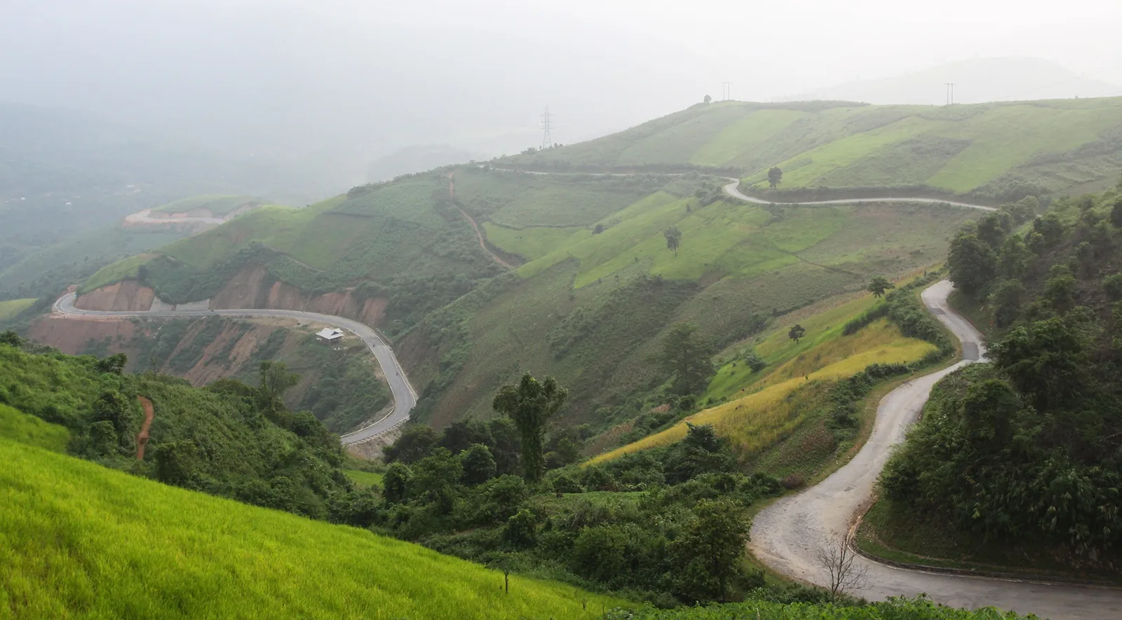 A winding mountain road curves through misty green hills at Pha Din Pass in Dien Bien.