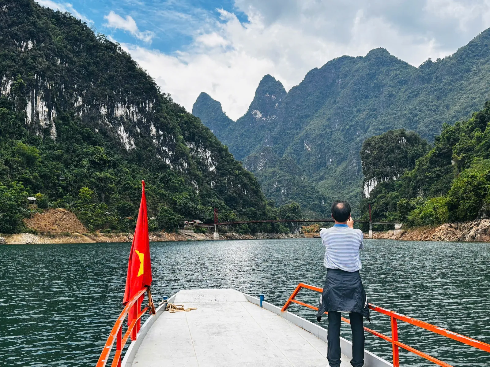 A traveler photographs limestone karst mountains from a boat with a Vietnamese flag on a river in Dien Bien.
