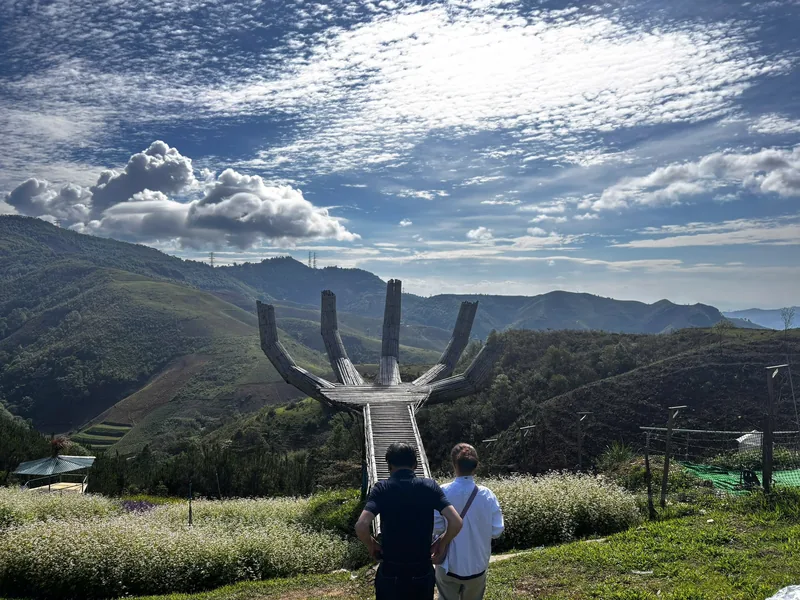 Two visitors admire a hand-shaped viewpoint overlooking green hills near Dien Bien Phu.
